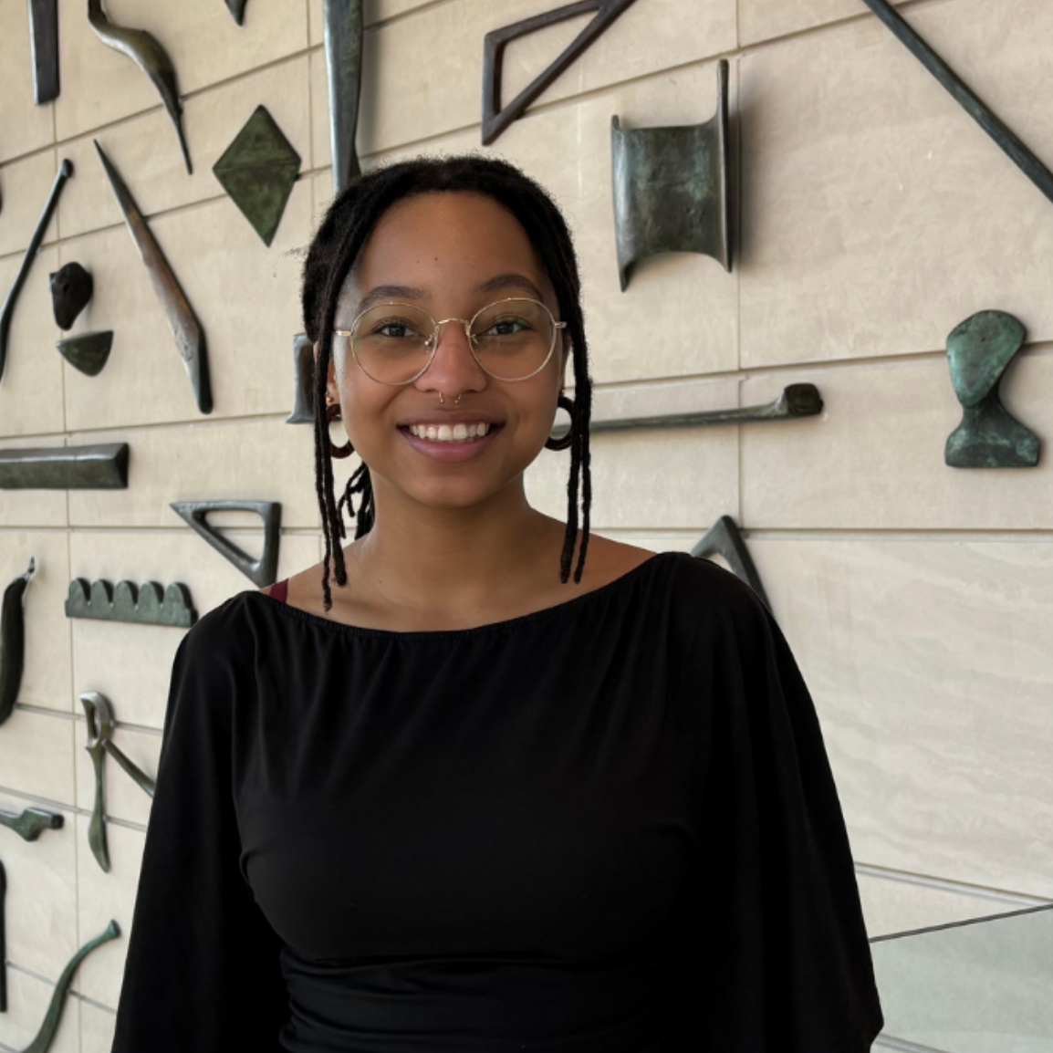 person in glasses stands in front of sculpture wall in Block atrium