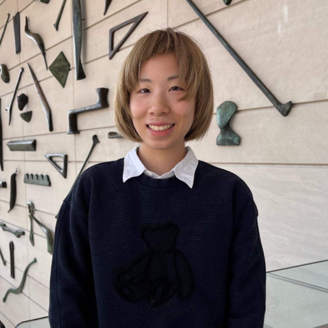 Block Curatorial Intern Muyang Chen stands in front of sculpture wall in museum atrium