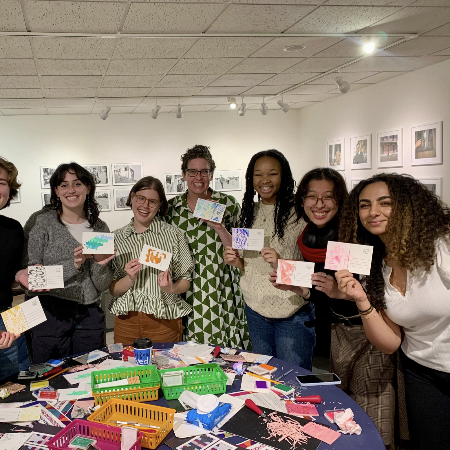 group of smiling people stand around table covered in art supplies holding postcards