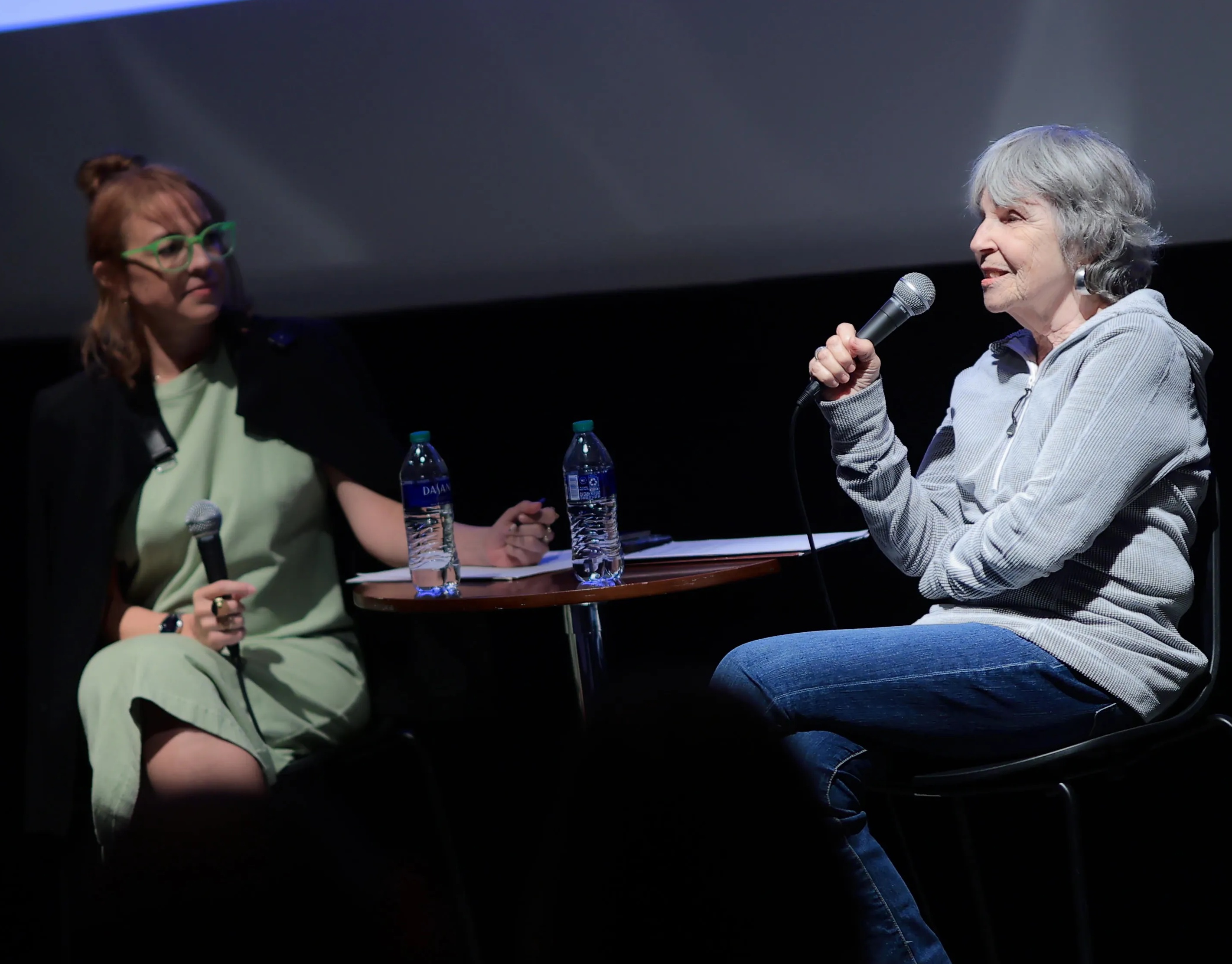 Ruslana Lichtzier and Bev Grant sit opposite each other in the Block Auditorium holding microphones