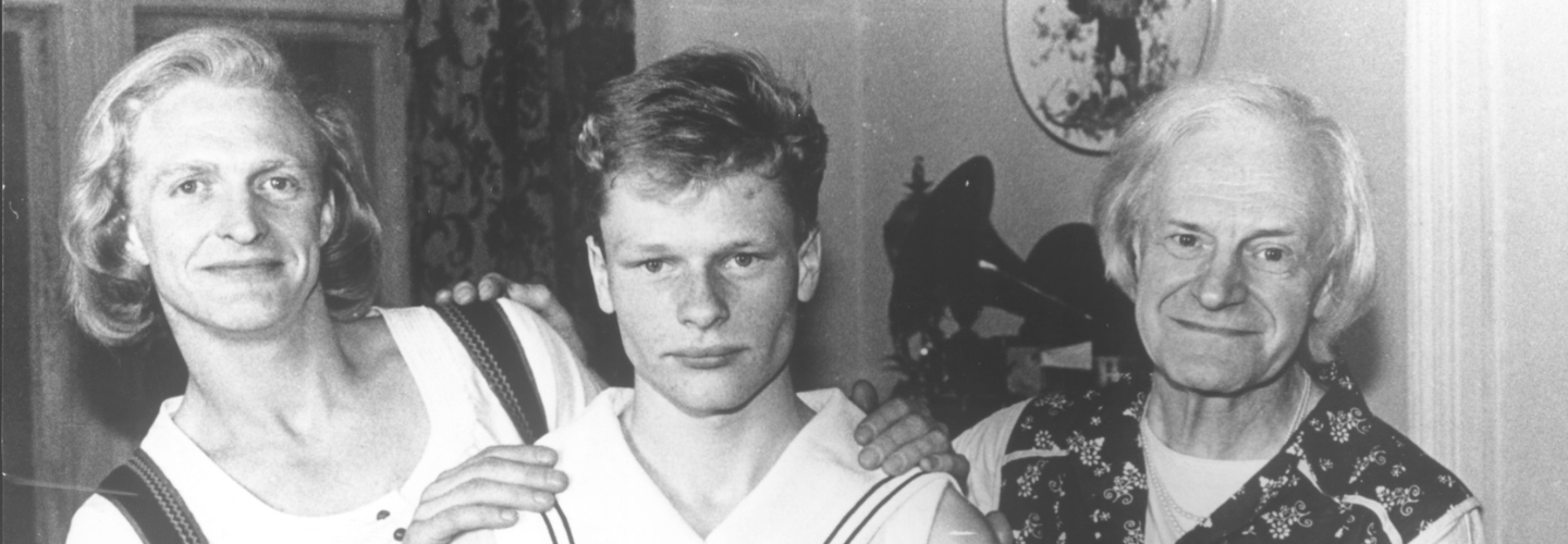 Black and white image of three people facing the camera, hands on each other's shoulders