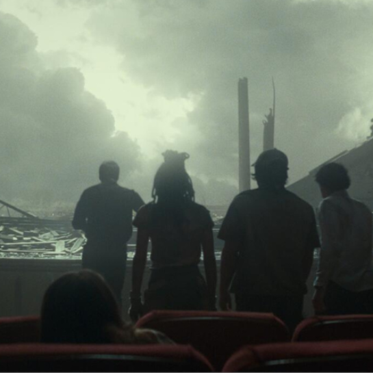 still from the 2024 film Twisters, in which a group of people look at stormclouds through the broken down wall of a movie theater auditorium