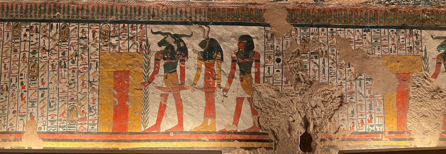 a wall with three Egyptian figures, two of whom have animal heads, and hieroglyphics surrounding