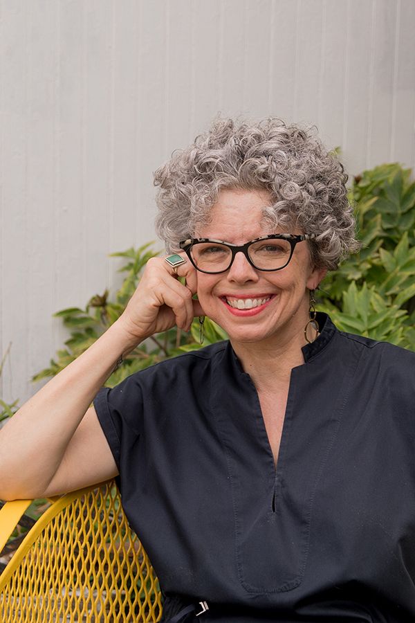photo of a white woman with curly grey, short hair and glasses, smiling while outside