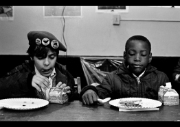 photograph of two kids eating food, one wears a beret with Black Panther Party and United Farm Worker pins