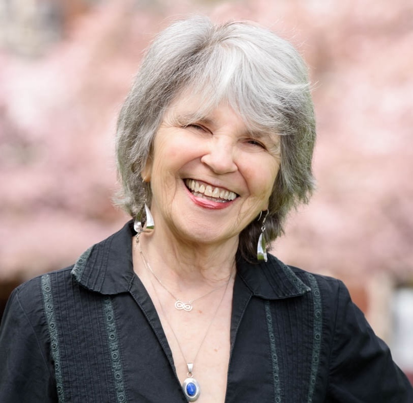 portrait photograph of white woman with short grey hair standing outside and wearing black button down 