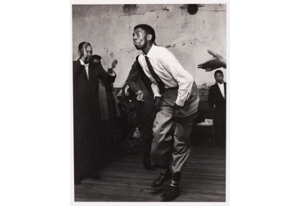 Black-and-white photo of an African-American man dancing and people around him clapping
