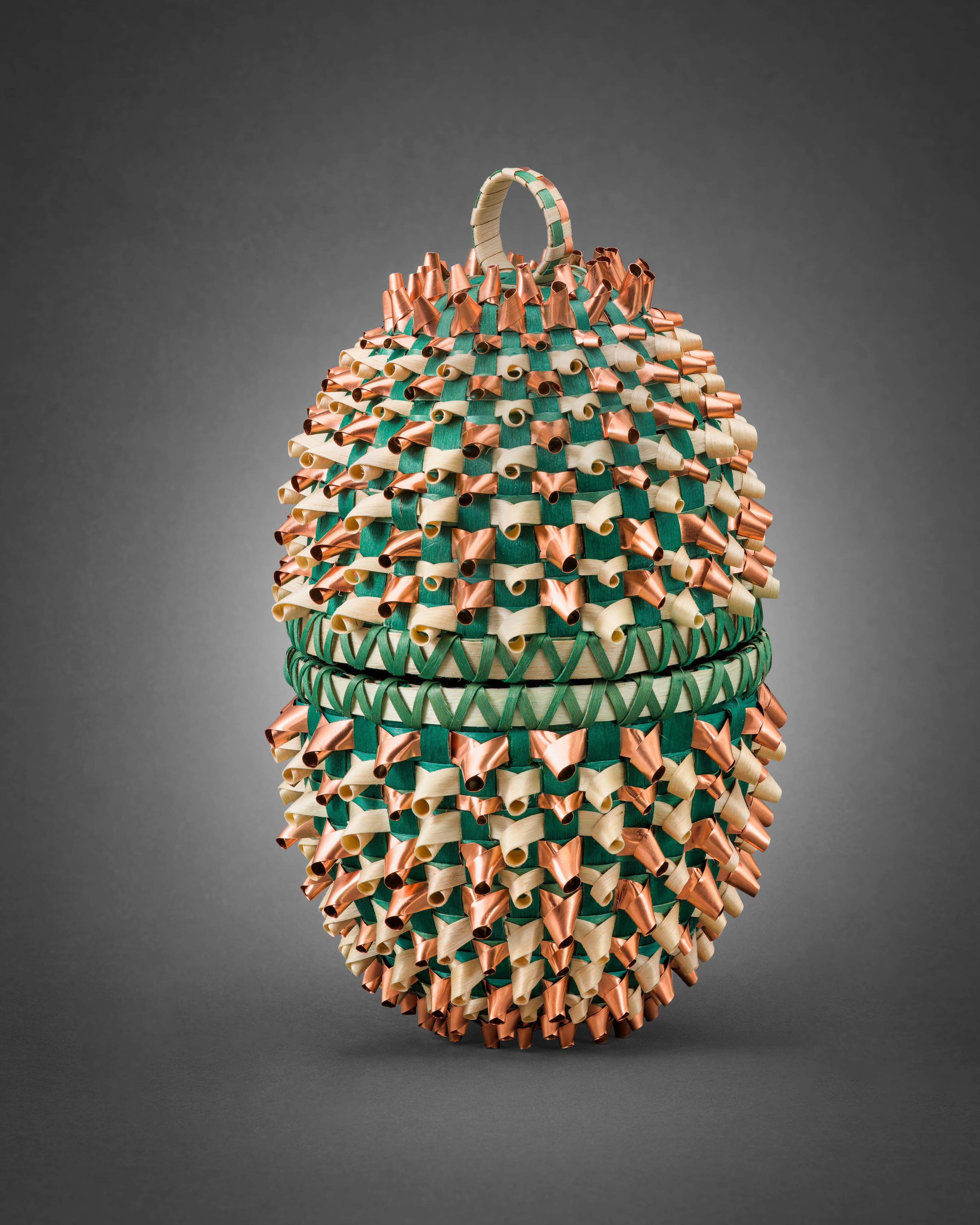 A woven basket with green, copper, and bronze-colored features