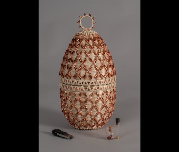 A woven basket with green, copper, and bronze-colored features