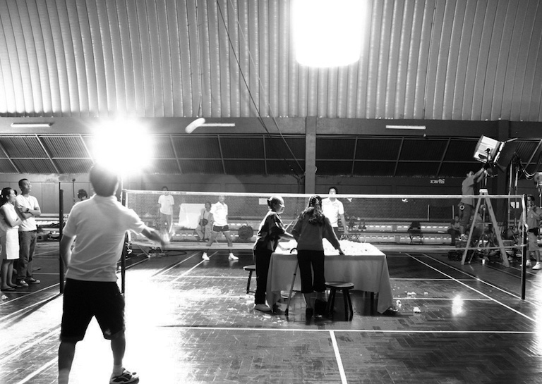 A film crew prepares a table inside a brightly-lit gymnasium