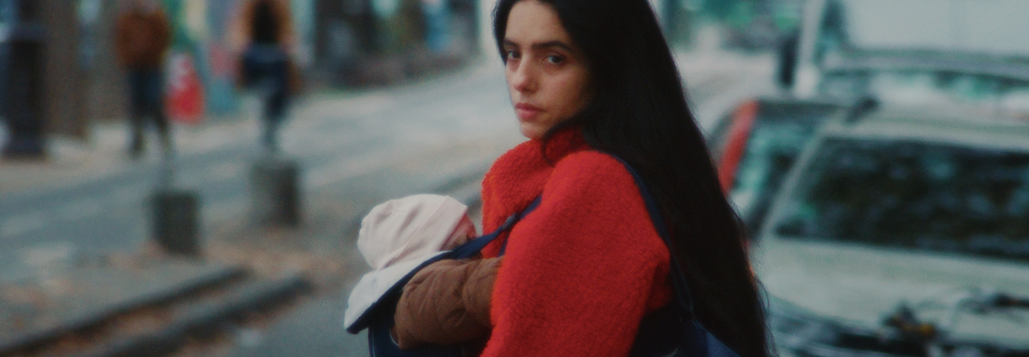 A woman with dark hair and a red coat holds a baby