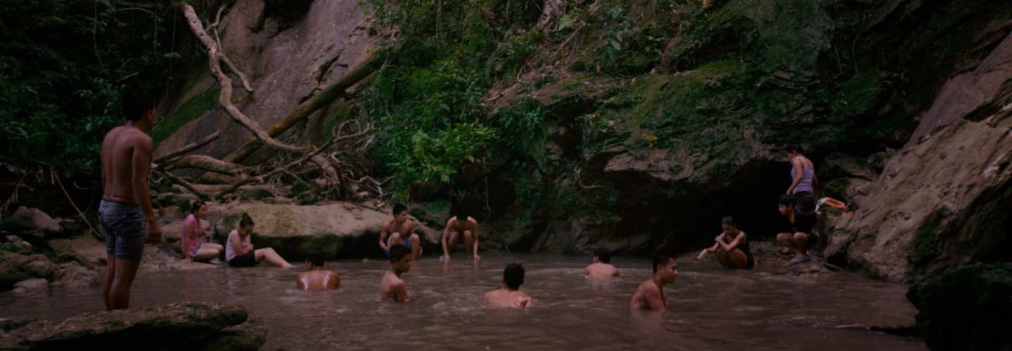 People swimming in a pond alongside greenery and rock