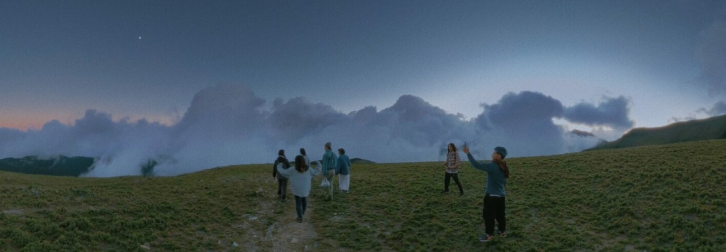 A group of people on a grassy hilltop up in the clouds