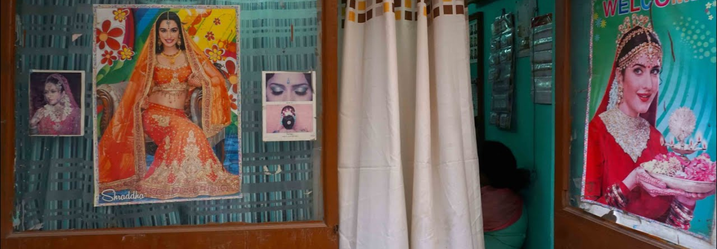 A colorful interior room with curtain draw, nearby are posters featuring women in sarees