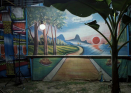 Painted theater backdrops of a rural Thai landscape and setting sun are illuminated by a globe light