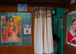 A colorful interior room with curtain draw, nearby are posters featuring women in sarees