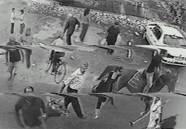 A black-and-white surveillance image of a people in a parking lot 