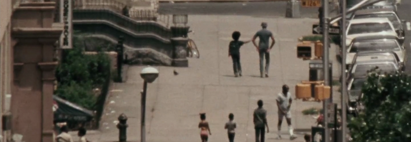 An adult man and a preadolescent child walk side by side on a city street.