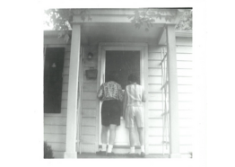 black and white photo of 2 women standing outside a house door, backs turned towards the camera