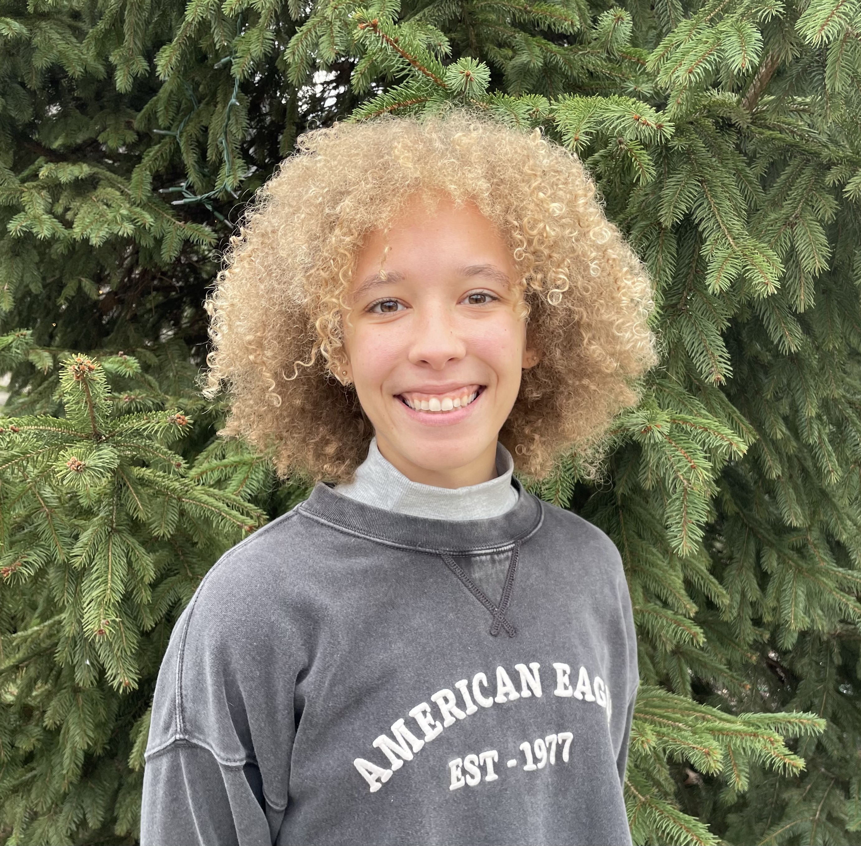 Black woman with light skin, tight blond curls, and grey sweater