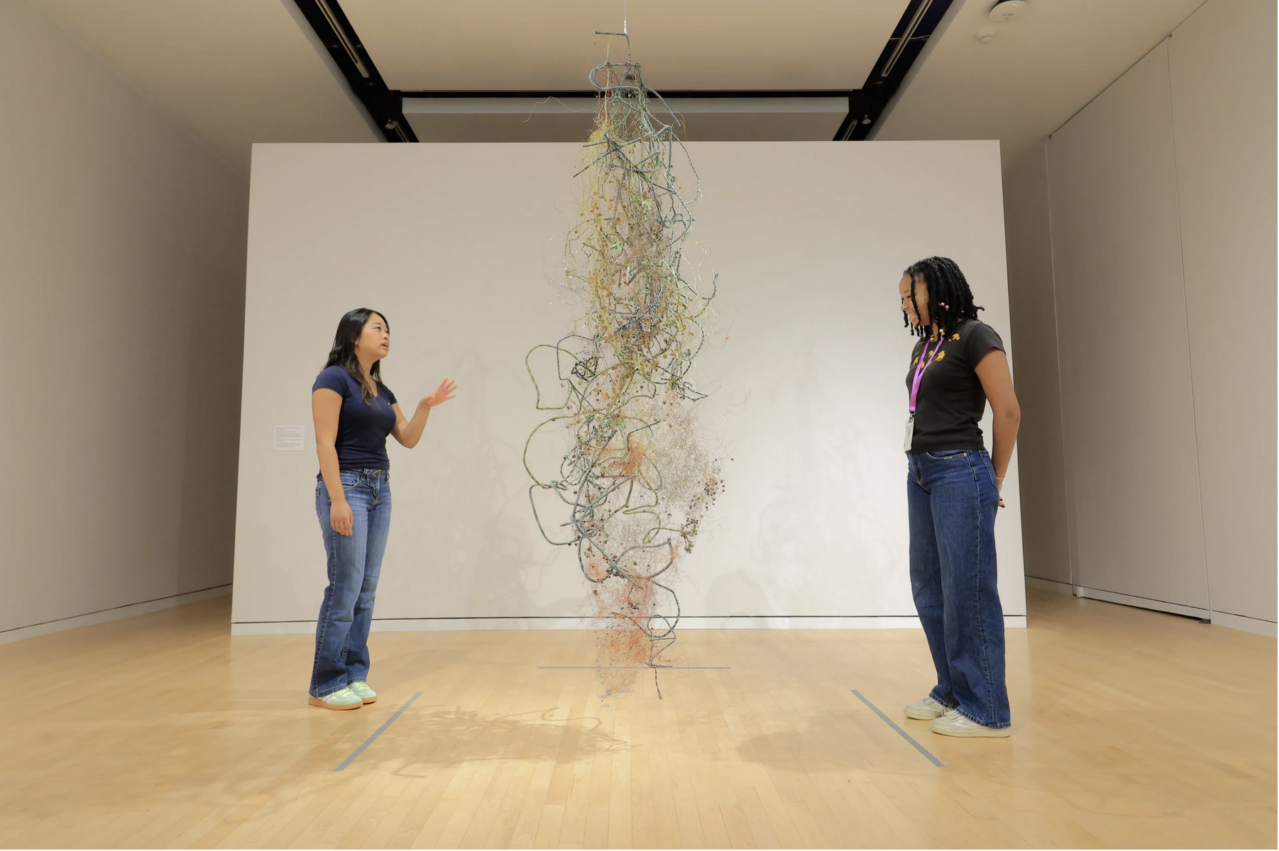 two people stand on opposite side of sculptural mass of wires suspended in museum gallery