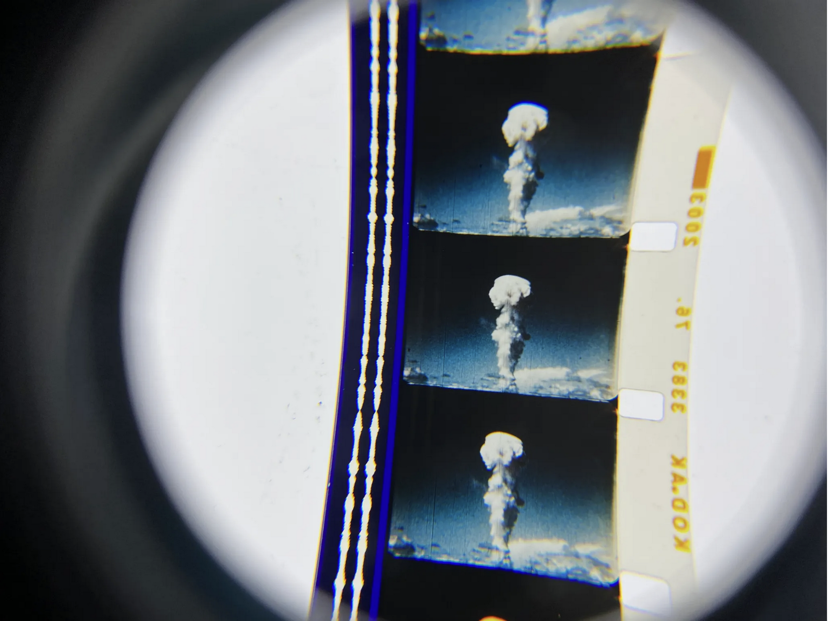 Three frames of a film strip, viewed in close up, show the mushroom cloud of a nuclear explosion